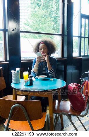 Stock Image - Woman using cellphone by cafe window, London, UK. Fotosearch
