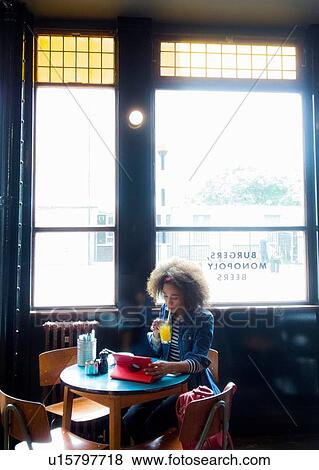 Stock Photo - Woman using digital tablet by cafe window, London, UK. Fotosearch