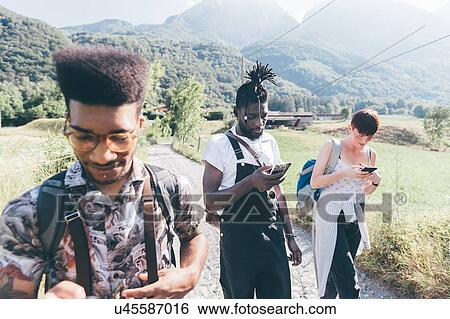 Stock Photograph - Young adult hikers on rural dirt track looking at smartphones, Primaluna, Trentino-Alto Adige, Italy. Fotosearch
