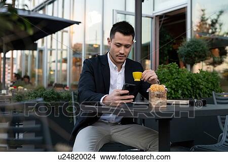 Picture - Young businessman at sidewalk cafe looking at smartphone, Milan, Italy. Fotosearch