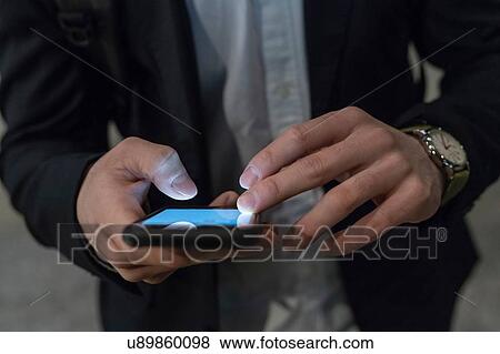 Stock Photo - Young businessman in city at night looking at smartphone, mid section, Milan, Italy. Fotosearch