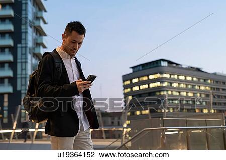 Young businessman in city looking at smartphone, Milan, Italy View Large Photo Image Stock Image - Young businessman in city looking at smartphone, Milan, Italy. Fotosearch