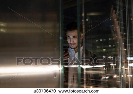 Young businessman in office building at night looking at smartphone, window view, Milan, Italy View Large Photo Image Stock Image - Young businessman in office building at night looking at smartphone, window view, Milan, Italy. Fotosearch