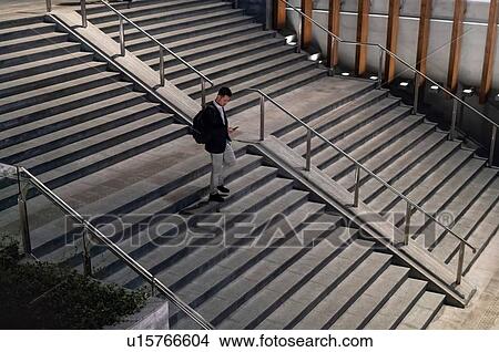 Young businessman moving down city stairway at night looking at smartphone, high angle view, Milan, Italy View Large Photo Image Picture - Young businessman moving down city stairway at night looking at smartphone, high angle view, Milan, Italy. Fotosearch