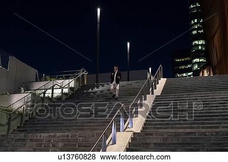 Stock Photo - Young businessman moving up city stairway at night, Milan, Italy. Fotosearch