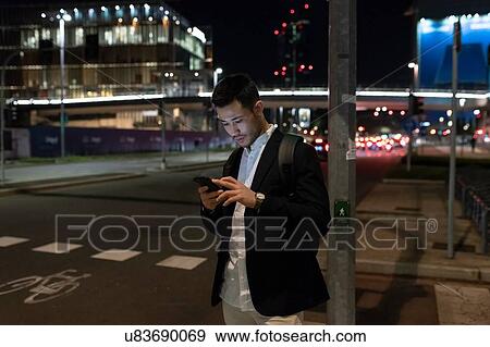 Young businessman on city street at night looking at smartphone, Milan, Italy View Large Photo Image Stock Photo - Young businessman on city street at night looking at smartphone, Milan, Italy. Fotosearch