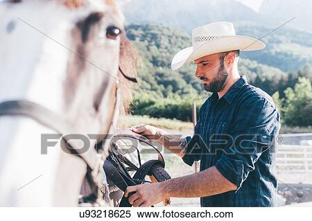 Young cowboy saddling horse in rural equestrian arena View Large Photo Image Stock Photography - Young cowboy saddling horse in rural equestrian arena. Fotosearch