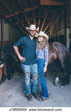 Stock Photo - Young cowgirl and boyfriend at stable entrance, portrait. Fotosearch