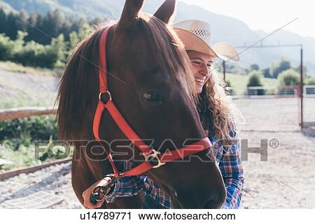 Stock Image - Young cowgirl leading horse in rural equestrian arena. Fotosearch
