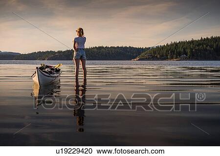Stock Image - Young female kayaker standing looking out over lake, Quadra Island, Campbell River, Canada. Fotosearch