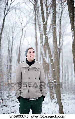 Stock Photography - Young man standing in snow covered forest, Ontario, Canada. Fotosearch