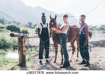 Stock Photograph - Young woman and men bonding with horse in rural equestrian arena, Primaluna, Trentino-Alto Adige, Italy. Fotosearch