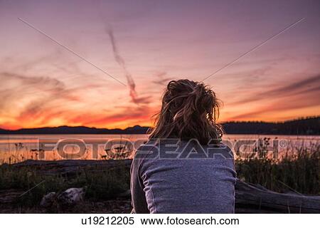 Stock Photography - Young woman looking out at sunset, rear view, Quadra Island, Campbell River, Canada. Fotosearch