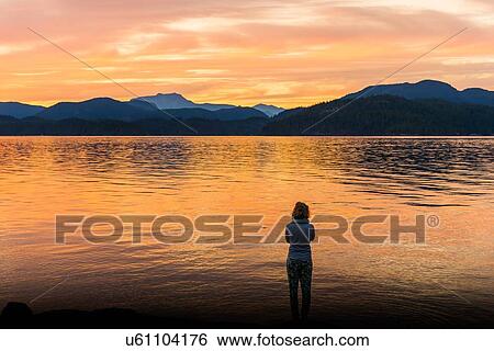 Stock Photograph - Young woman looking out at sunset, Quadra Island, Campbell River, Canada. Fotosearch