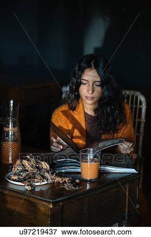 Stock Photo - Young woman sitting at table looking at book. Fotosearch