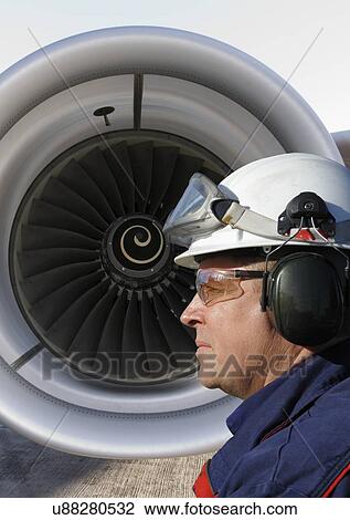 Stock Image - Airplane mechanic standing in front of a jumbo jet's engine.. Fotosearch