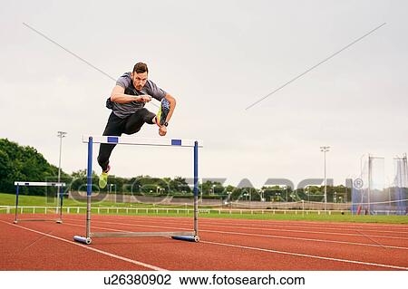 Athlete jumping over hurdle on running track View Large Photo Image Stock Image - Athlete jumping over hurdle on running track. Fotosearch