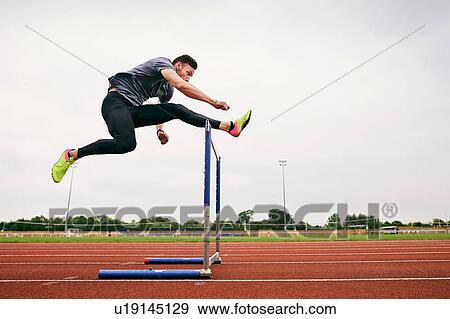 Athlete jumping over hurdle on running track View Large Photo Image Stock Photo - Athlete jumping over hurdle on running track. Fotosearch