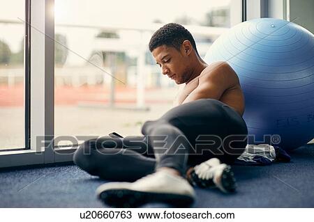 Stock Image - Athlete texting while resting beside exercise ball. Fotosearch