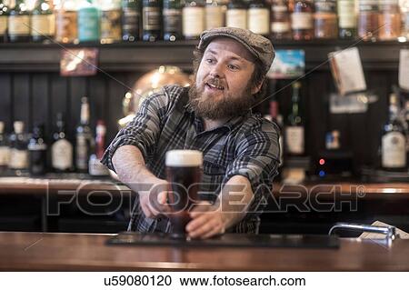 Stock Image - Barman serving beer from bar in traditional Irish public house. Fotosearch