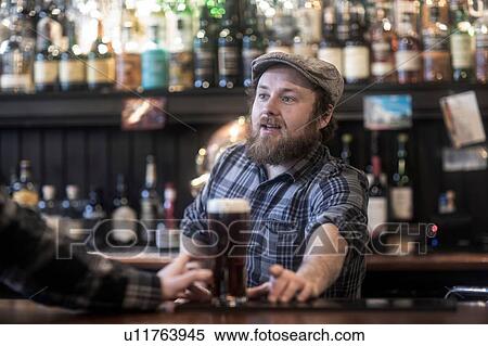 Stock Photography - Barman serving beer to customer at bar in traditional Irish public house. Fotosearch