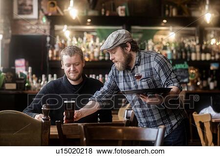 Barman serving beer to customer in traditional Irish public house View Large Photo Image Stock Photo - Barman serving beer to customer in traditional Irish public house. Fotosearch