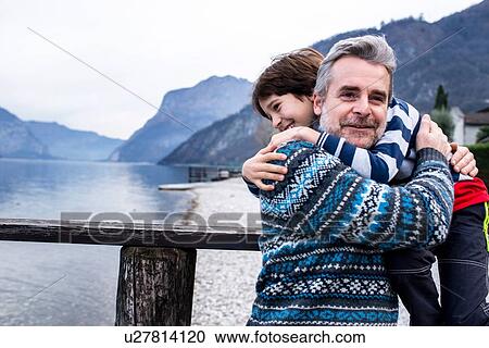 Stock Image - Boy and father hugging each other on lakeside pier, Lake Como, Onno, Lombardy, Italy. Fotosearch