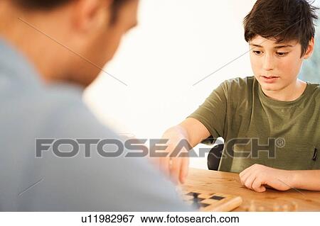 Boy and father playing chess at living room table, over shoulder view View Large Photo Image Stock Photo - Boy and father playing chess at living room table, over shoulder view. Fotosearch