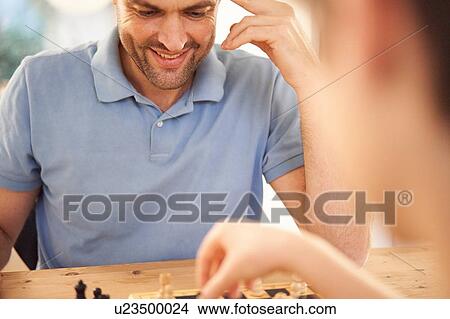 Picture - Boy and father playing game of chess at living room table, over shoulder close up. Fotosearch