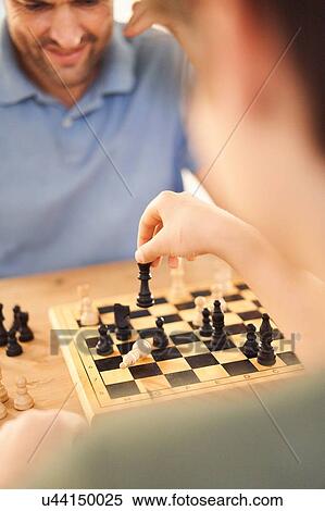 Boy and father playing game of chess at living room table, over shoulder close up View Large Photo Image Stock Photography - Boy and father playing game of chess at living room table, over shoulder close up. Fotosearch