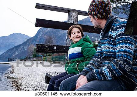 Stock Photography - Boy and father sitting chatting on lakeside pier, Lake Como, Onno, Lombardy, Italy. Fotosearch