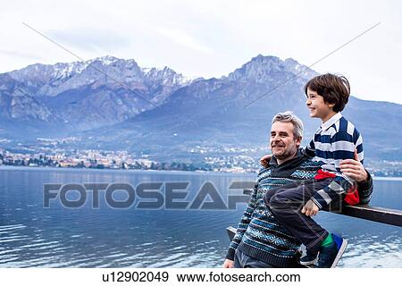 Stock Photo - Boy and father sitting on pier fence, Lake Como. Onno, Lombardy, Italy. Fotosearch