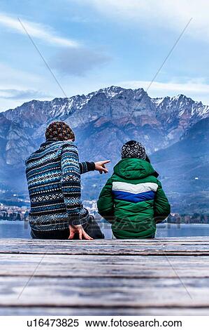 Boy and father sitting pointing on lakeside pier, rear view, Lake Como, Onno, Lombardy, Italy View Large Photo Image Stock Photography - Boy and father sitting pointing on lakeside pier, rear view, Lake Como, Onno, Lombardy, Italy. Fotosearch