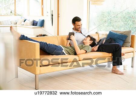 Boy and father using digital tablets whilst relaxing on sofa View Large Photo Image Stock Image - Boy and father using digital tablets whilst relaxing on sofa. Fotosearch