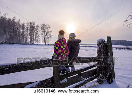 Boy and girl sitting on fence in snow covered landscape, rear view View Large Photo Image Stock Photograph - Boy and girl sitting on fence in snow covered landscape, rear view. Fotosearch