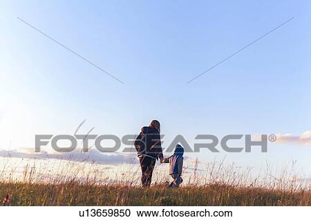 Stock Image - Boy and mother walking hand in hand on rural hilltop. Fotosearch