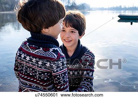 Stock Image - Boy and toddler brother in matching sweaters on lakeside, Lake Como, Lecco, Lombardy, Italy. Fotosearch