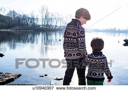 Stock Photo - Boy and toddler brother in matching sweaters standing on lakeside, Lake Como, Lecco, Lombardy, Italy. Fotosearch