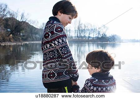 Stock Photo - Boy and toddler brother in matching sweaters holding hands on lakeside, Lake Como, Lecco, Lombardy, Italy. Fotosearch
