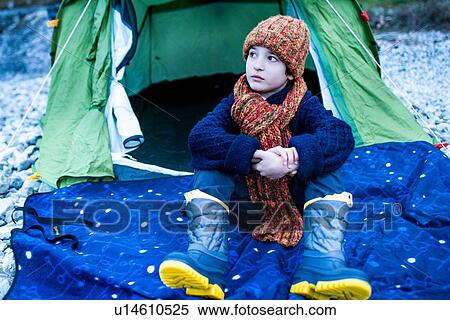 Stock Photography - Boy in knitted hat sitting outside tent on lakeside, Lake Como, Onno, Lombardy, Italy. Fotosearch