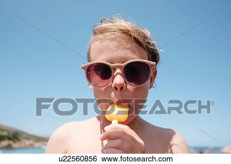 Stock Photograph - Boy in sunglasses enjoying ice lolly. Fotosearch