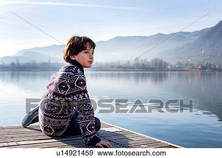 Stock Photo - Boy looking back from lakeside pier, Lake Como, Lecco, Lombardy, Italy. Fotosearch