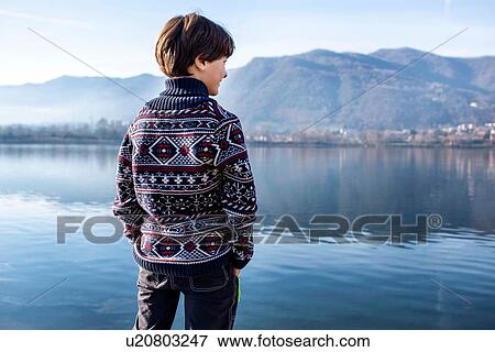 Stock Photo - Boy looking out from lakeside, rear view, Lake Como, Lecco, Lombardy, Italy. Fotosearch