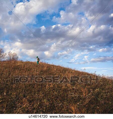 Stock Image - Boy on rural hillside looking down. Fotosearch