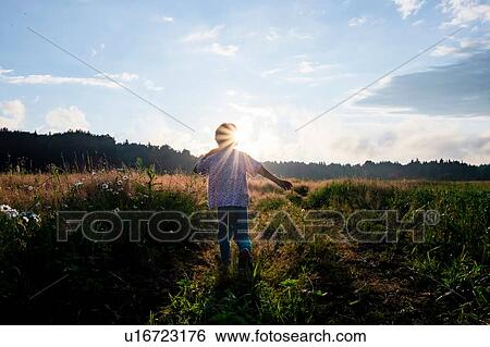 Stock Photograph - Boy playing in field at sunset, rear view. Fotosearch