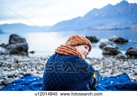 Stock Photography - Boy sitting on blanket on lakeside, Lake Como, Onno, Lombardy, Italy. Fotosearch