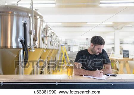 Stock Image - Brewer ordering ingredients on phone in small brewery. Fotosearch