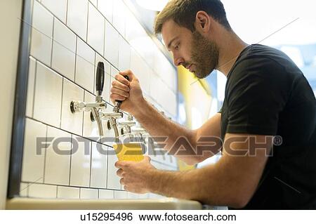 Stock Photograph - Brewer pouring beer in small brewery. Fotosearch