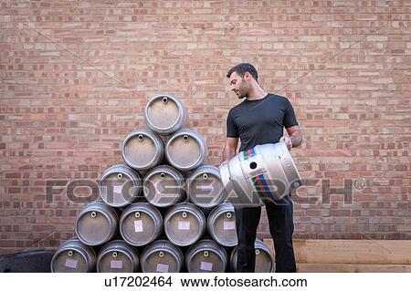 Picture - Brewer stacking barrels in small brewery. Fotosearch