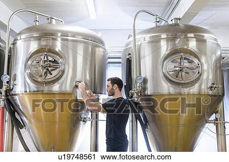 Stock Image - Brewer taking a sample of beer in small brewery. Fotosearch